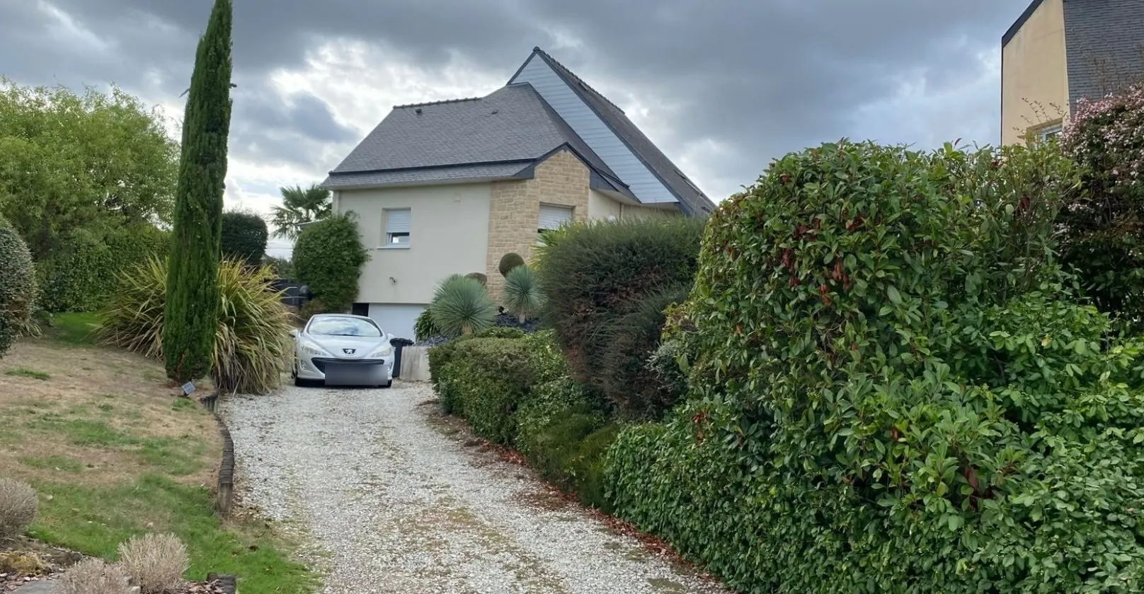 Avant : allée de gravillons, haie de photinias et voiture garée devant la maison
